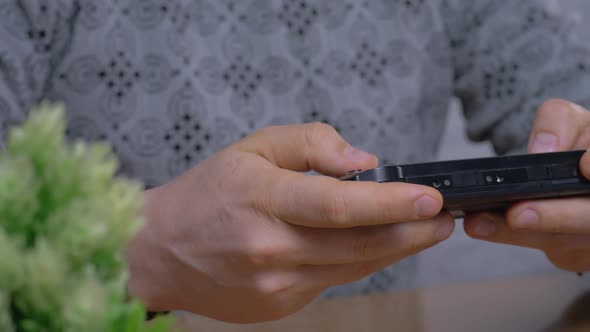 Unrecognizable Man in Gray Sweater Play on Plastic Handheld Game Console