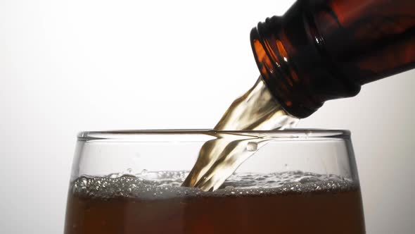 Beer is pouring with bubbles and foam in large beer glass from bottle on white background close up. alt