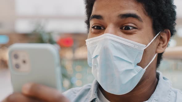 African American Masked Guy Man in Medical Mask Surprised Message Received Wins Online Bets Looking alt