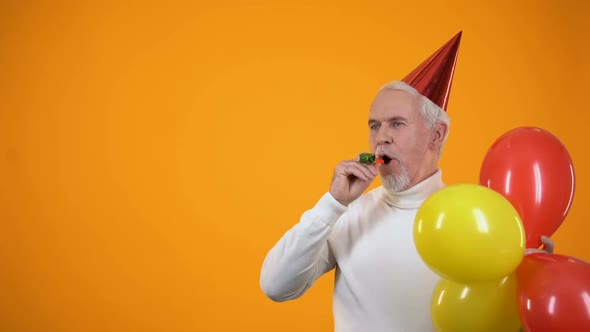Cheerful Senior Man With Colorful Balloons Using Party Blower, Event Agency alt