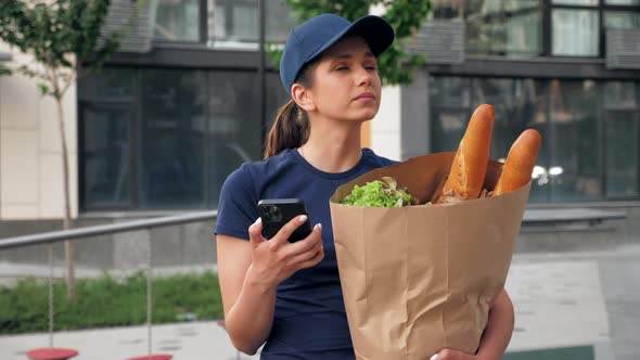 Food Delivery Woman Courier Uses Smartphone Holds Paper Bag Looking Address alt