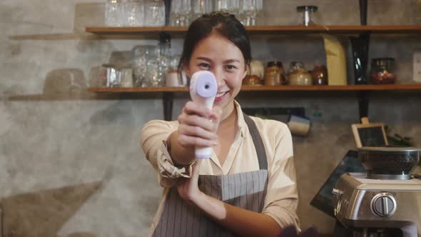 Asia female restaurant staff using infrared thermometer checker or temperature gun on customer's . alt