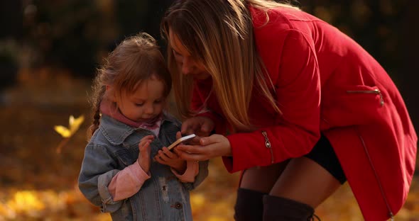 Cute Little Girl in Black Jacket Looks at the Yellow Leaves and Rejoices in the Autumn Park with Her