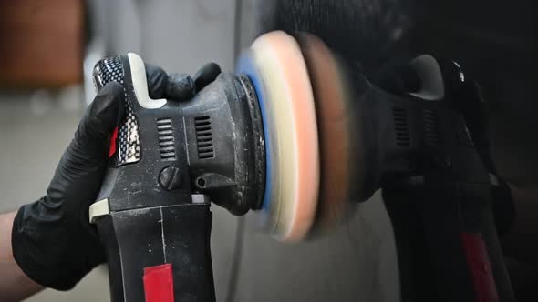 Hands of Male Mechanic Using a Polishing Machine To Polish a Black Car Body alt