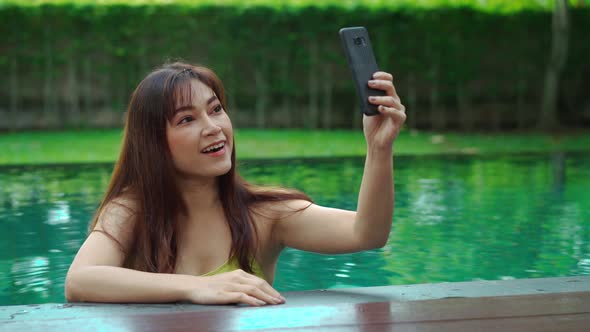 happy woman using smartphone to selfie a photo in swimming pool