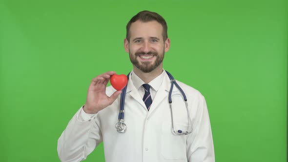 Young Male Doctor Holding a Heart Shape and Smiling Against Chroma Key alt