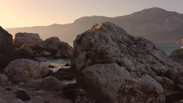 Beautiful Rocky Cliffs and Clear Ocean Water with Mountains in the Background alt