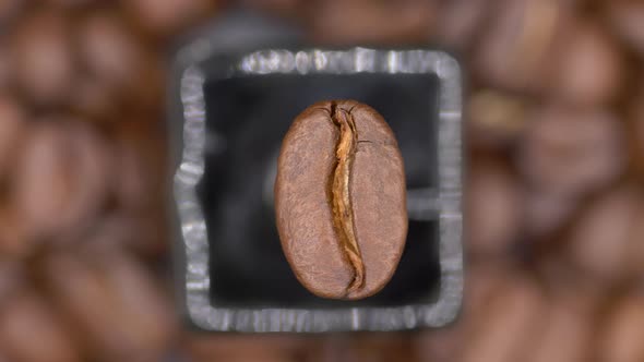 Top View Of A Roasted Arabica Coffee Bean Rotating Against Blurry Coffee Beans Backdrop. close up alt