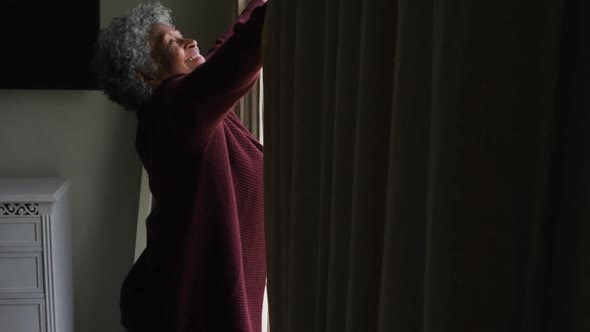 Senior african american woman opening curtains of the window at home alt