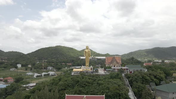 Drone Flying backwards from Golden standing Buddah Statue at Wat Khao Noi temple, Hua Hin. Thailand alt