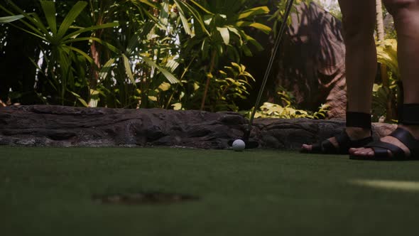 A Young Woman Playing Mini Golf. Legs in the Frame. Mid Shot. Shoot Ball in the Hole