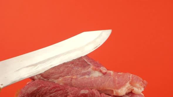 The concept of cutting fresh meat. A sharp large knife plunges and cuts a piece of red raw meat. alt