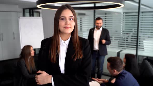 Businesswoman at the Camera. She Stands with Her Arms Crossed in Front of Her Colleagues, Who Are