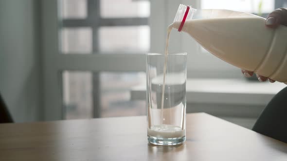 Woman Pours Milk From a Bottle Into a Glass Indoors Close Up Cinematic Shot