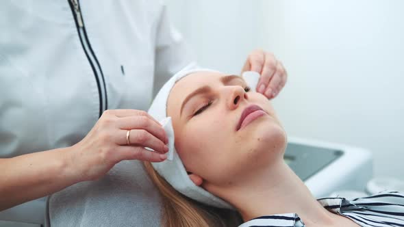 Cosmetologist Wiping Woman's Face with Cotton Pads alt