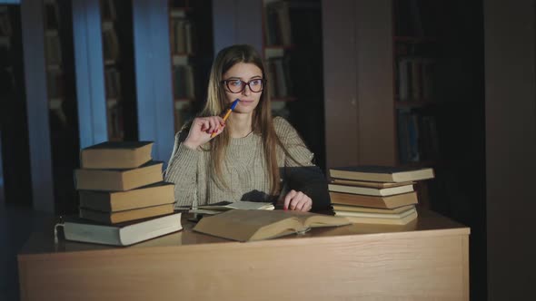 Diligent Student with Pen in Hand Thinking During Working with Books at the Desk alt
