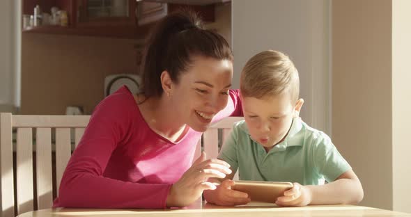Mother And Child Playing On A Mobile Phone At The Table Having A Good Time Together alt