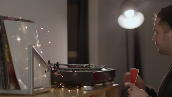 Unshaven Handsome Guy Puts Records on Turntable Listening to Music in Headphones