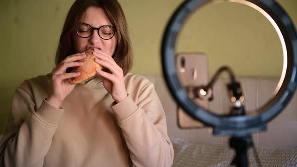 Girl food blogger bites a croissant and records a video blog alt
