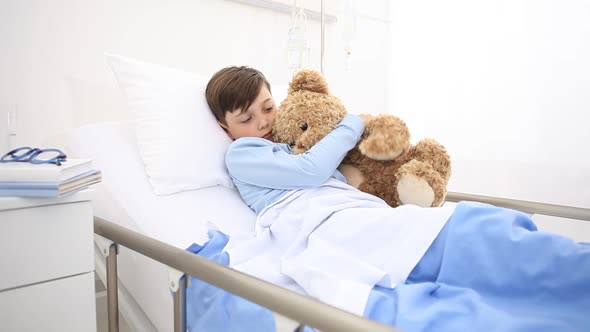 Child in hospital lying alone in bed play with teddy bear 