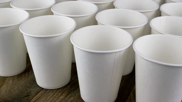 Row of White Disposable Paper Cup for Coffee or Hot Beverage on Dark Backdrop Rotate Slowly alt