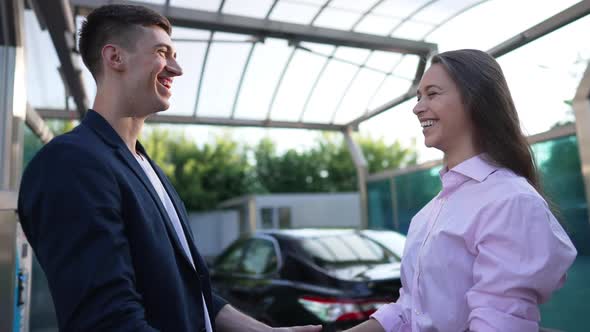 Side View Cheerful Young Couple Laughing Gesturing Highfive Standing at Clean Vehicle in Car Wash alt