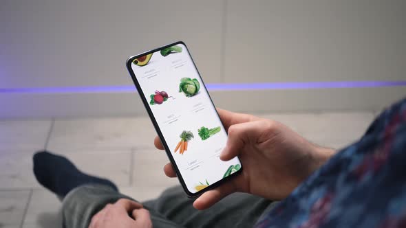 Man at home orders groceries online, using a food delivery app on a smartphone