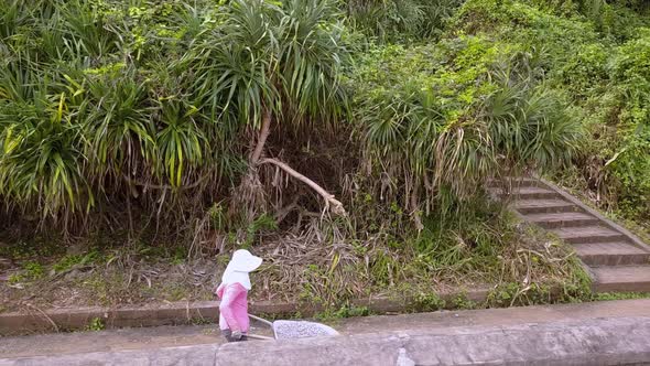 Woman with face covereding a wheelbarrow full of gravel on the island of Cat Ba Vietnam, Side view t alt