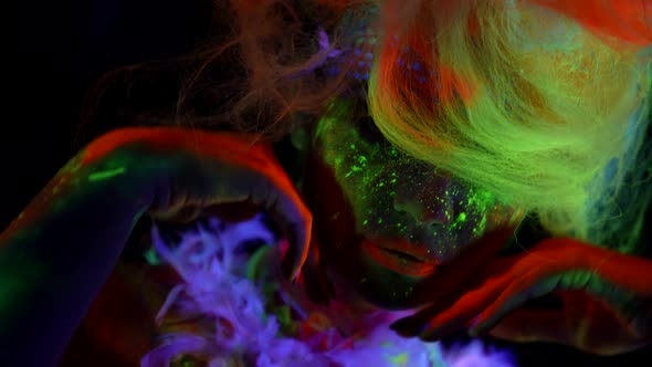 Ultraviolet Light on Face of Model with Fluorescent Makeup Bright Colors on Female Face in Darkness alt