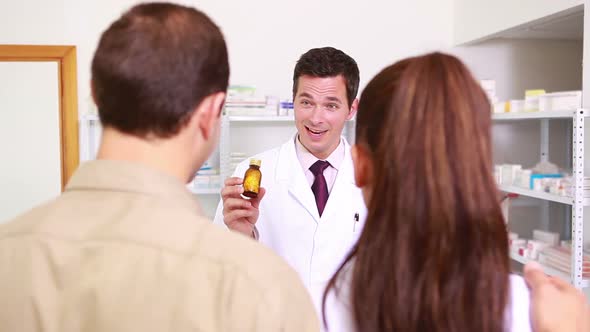 Pharmacist holding at a flask of pills to a man and a woman alt