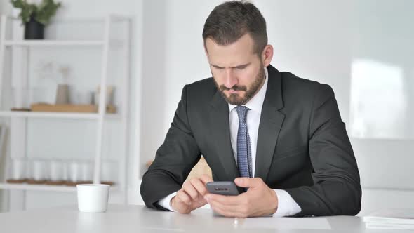 Tense Upset Businessman Reacting to Loss on Smartphone alt