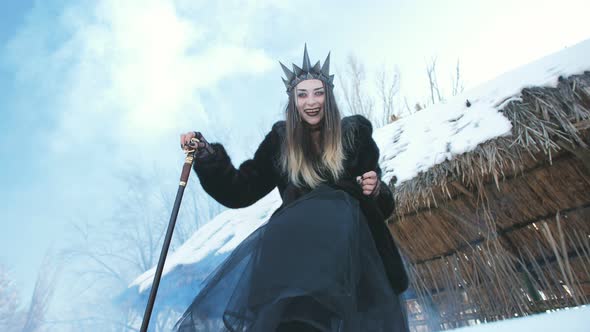 The Snow Queen in Black Clothes and with a Cane in Her Hands is Intimidating and Looks at the Camera alt