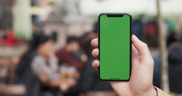 Closeup of a Man's Hand Holding a Mobile Telephone with a Vertical Green Screen on the Streets alt