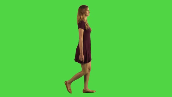 Casual Young Woman Walking While Looking Upwards Over a Green Screen alt