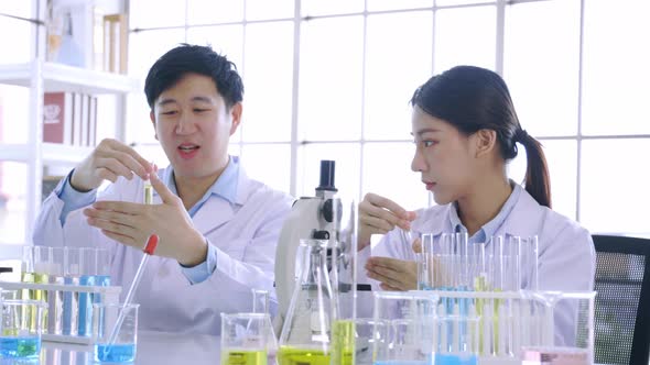 Young Asian Female Scientist Doing Research in Laboratory Wearing Lab Coat and Gloves with Colleague alt