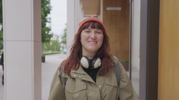 Portrait Woman in a Red Hat Listening to Music in Headphones in the City Walks alt
