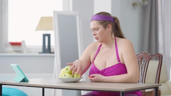 Sad Overweight Woman Eating Apple with Dissatisfied Facial Expression alt