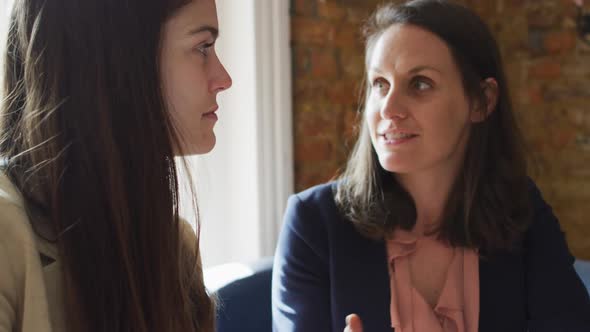 Portrait of two caucasian businesswomen sitting at table, talking, having business meeting alt
