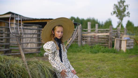 Rustic Girl in Vintage Dress and Hat on Haystack and Pitchfork Background in Countryside alt