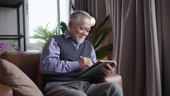 Asian mature senior man using tablet in living room at home.