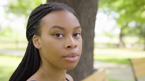A Young Black Woman Takes Off a Face Mask and Looks at the Camera As She Sits on a Bench alt