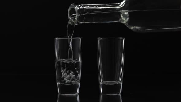 Pouring Up Two Shot of Vodka From a Bottle Into Glass, Black Background alt