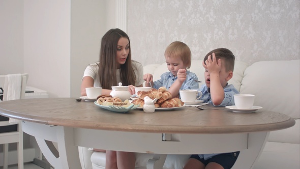 Young mother attending to her little boys having tea at home