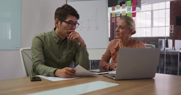 Diverse male and female business colleagues in discussion in meeting room using laptop alt