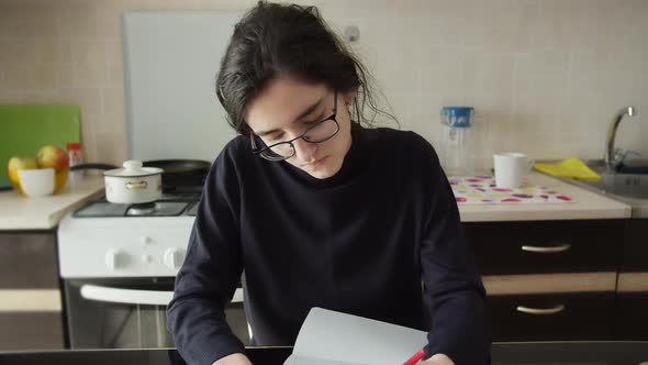 Serious Brunette Girl Draws on Paper in the Kitchen