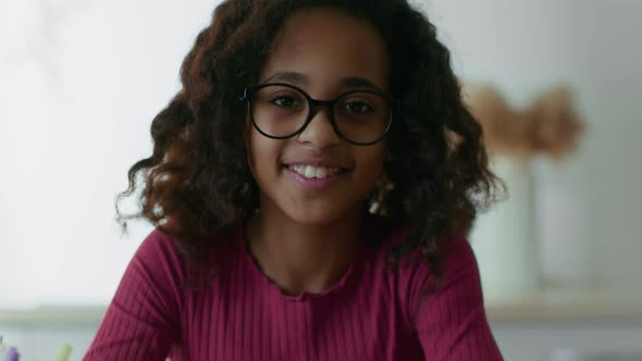 Smart Little African American Girl Wearing Eyeglasses Doing Hometask at Home Raising Head and alt