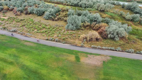 Mature couple riding bicycles along a nature trail by a calm river - aerial tracking view alt