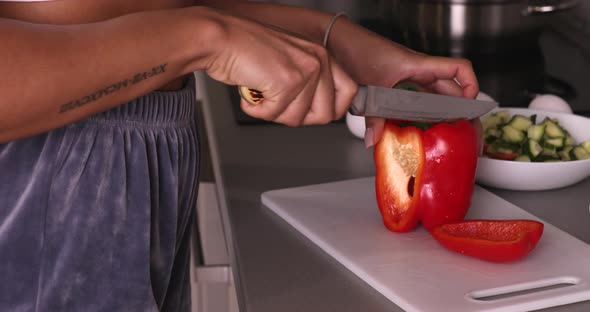 Black woman cutting red capsicum in slices on  chopping board.