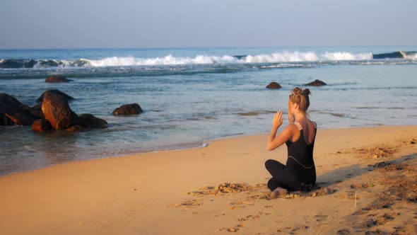 Young Blond Woman in Black Tracksuit Meditates in Yoga Pose alt