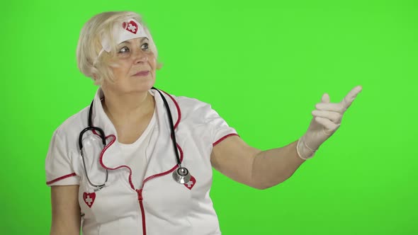 Elderly Caucasian Female Doctor Nurse Points at Something with Her Hands alt